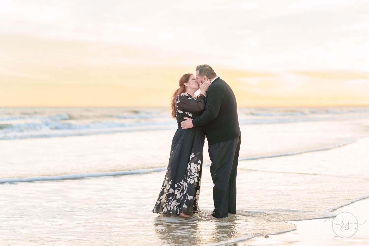 Couple kissing in the shallow surf under a soft golden sunset at Huntington Beach State Park