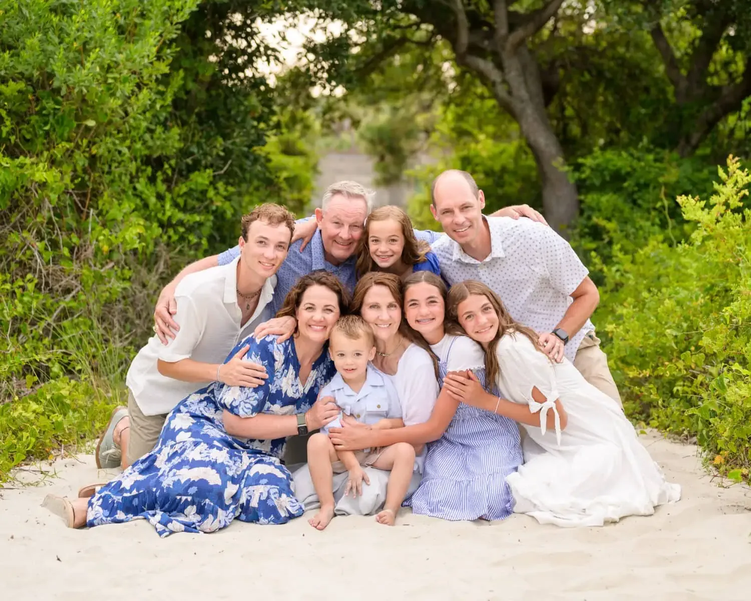 Big family with grandparents hugging close together on a sandy path under the trees at Huntington Beach State Park