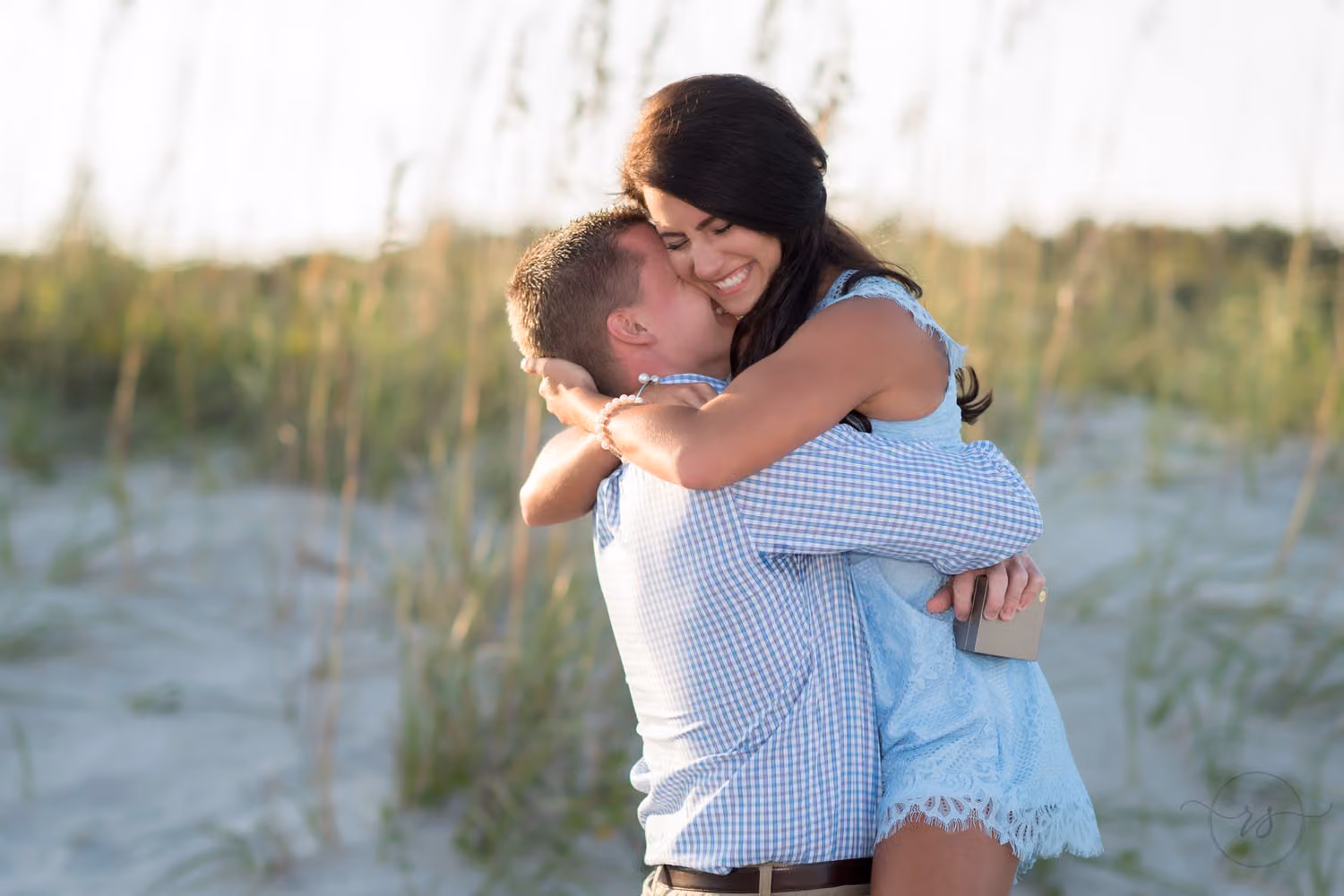 Newly engaged woman hugging her fiancé tightly in front of the sea oats at Myrtle Beach State Park