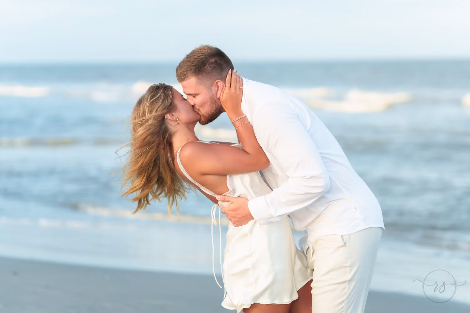 Close view of a newly engaged couple kissing in front of rolling waves in Pawleys Island