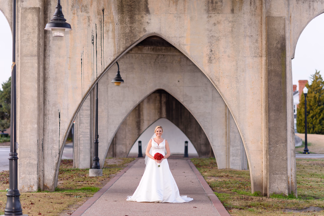 Bride standing on the path under the tall concrete arches of the old bridge at the Conway River Walk