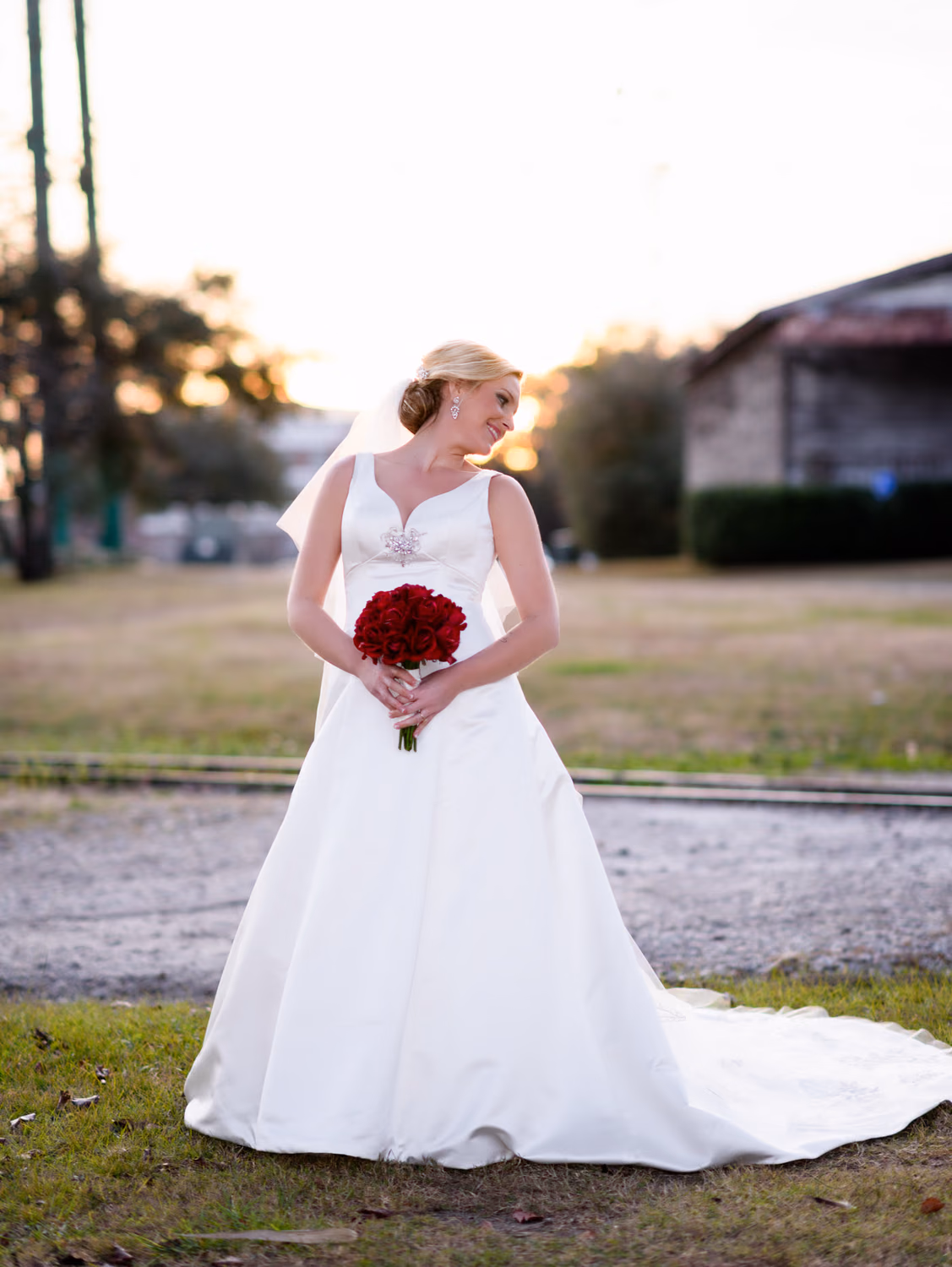 Bride glancing to the side with her red roses on the grass at the Conway River Walk