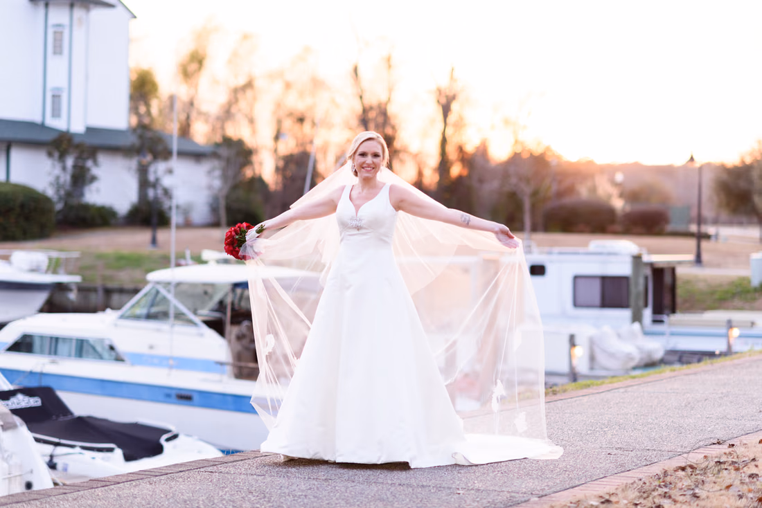 Bride holding her veil out wide at sunset with boats behind her at the Conway River Walk marina