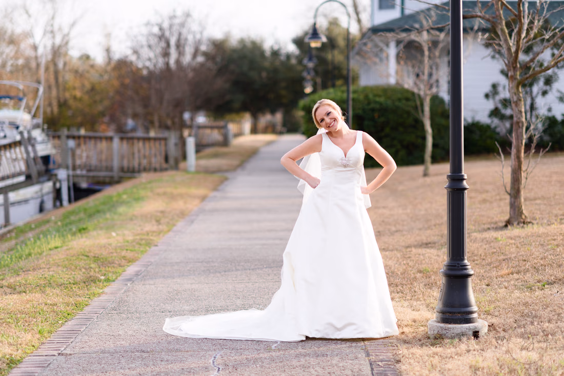 Bride with hands on her hips on the paved path by a lamp post at the Conway River Walk
