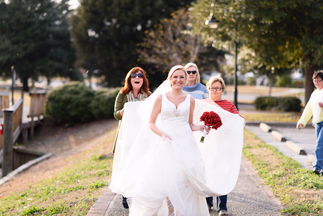 Women help carry the bride's train as she walks along the path at the Conway River Walk