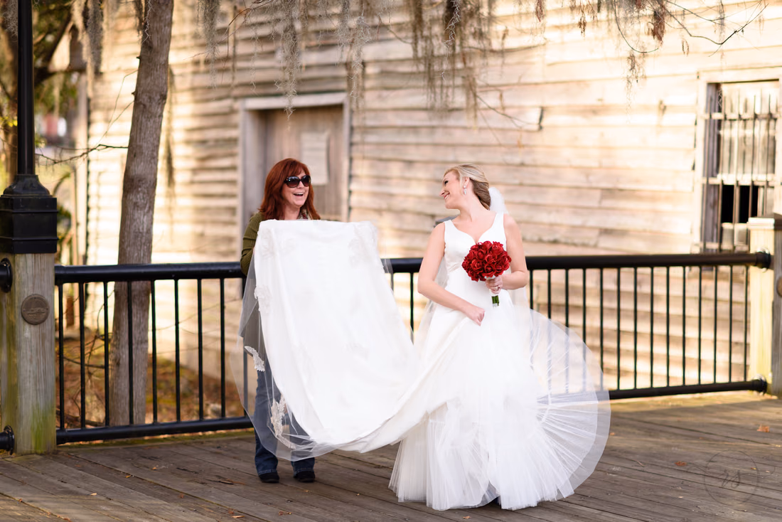 A woman lifts the bride's dress on the boardwalk by an old wooden building at the Conway River Walk