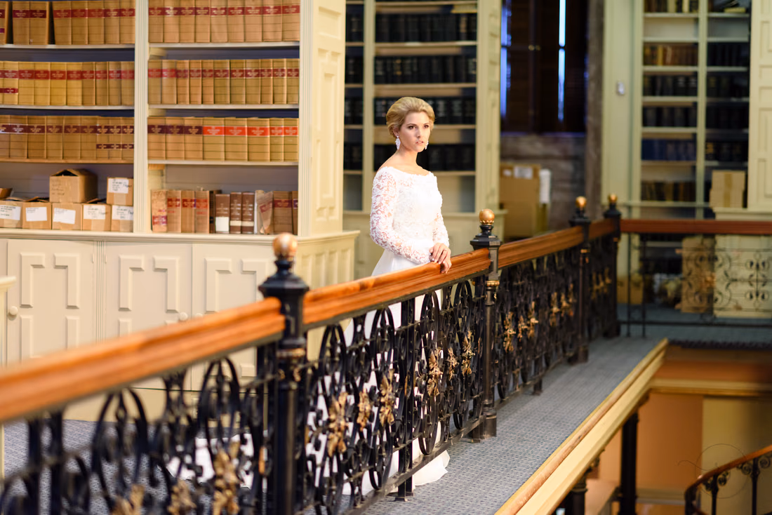 Bride behind an ornate iron and wood railing with shelves of law books at the South Carolina State House