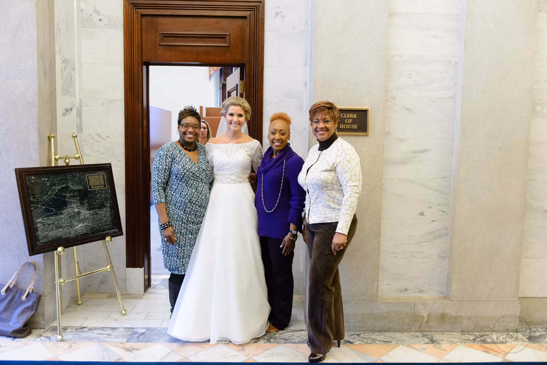 Bride posing with three women beside a marble wall and doorway inside the South Carolina State House