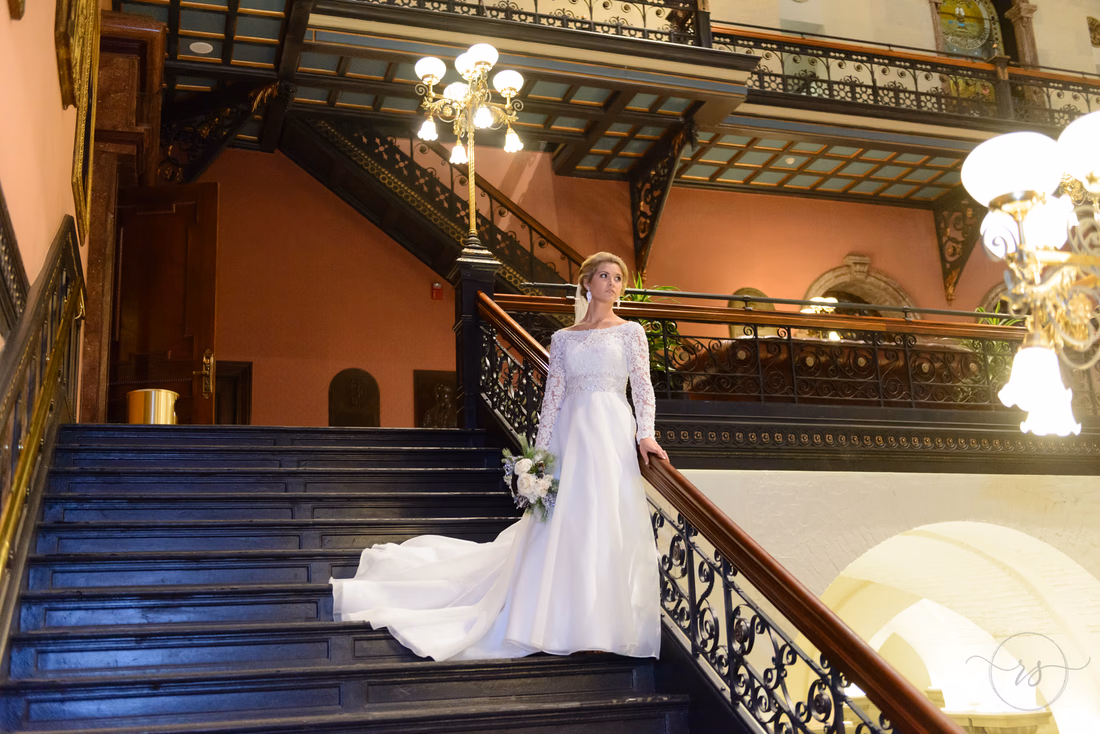 Bride standing on the grand staircase with iron railings and brass lamps inside the South Carolina State House