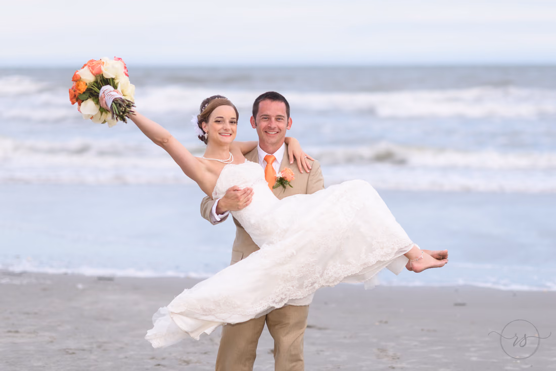Groom lifting up bride while she holds flowers in the air - Hilton Myrtle Beach Resort at Kingston Resorts