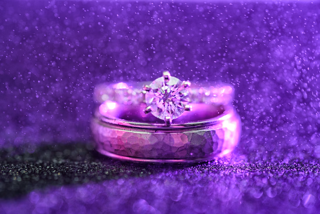 Engagement ring and wedding band lit purple on a glittery surface at Hilton Myrtle Beach Resort at Kingston Resorts