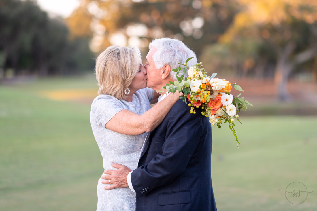Bride wraps her arms and bouquet around the groom's shoulders for a kiss at the Dunes Golf and Beach Club
