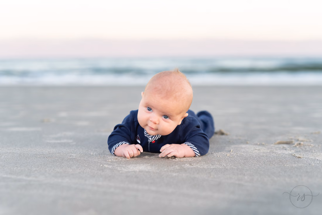Baby boy on his tummy in the sand by the ocean at Huntington Beach State Park