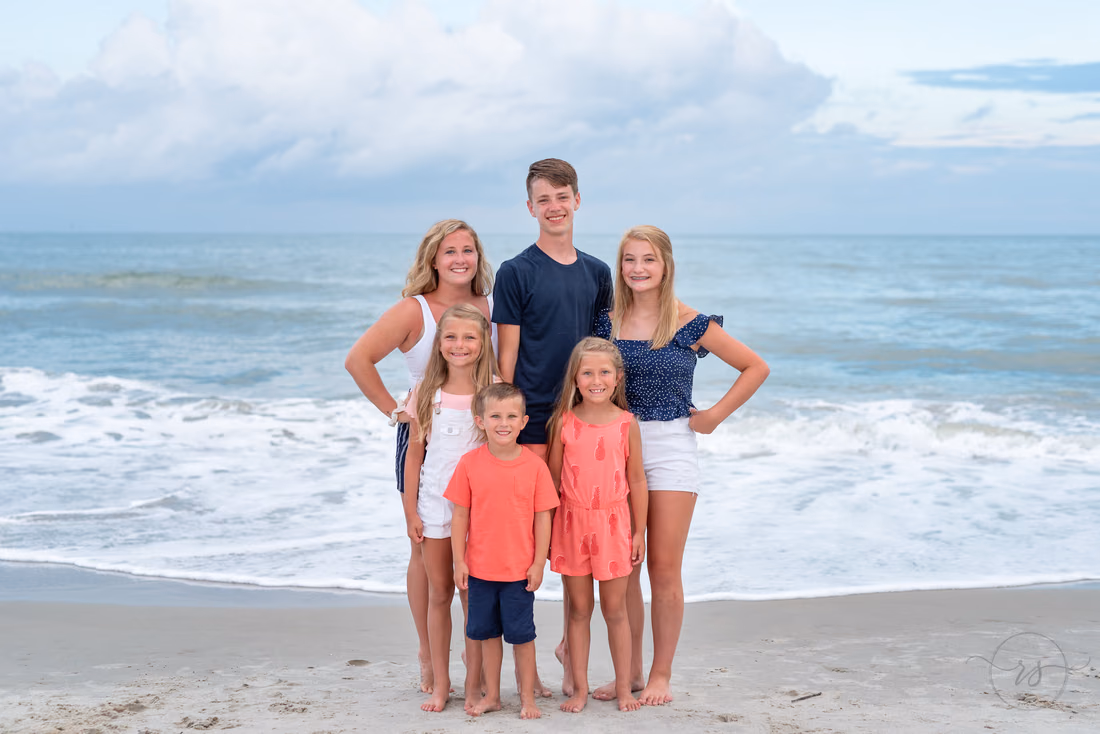 Family dressed in coral and navy standing by the waves at Huntington Beach State Park