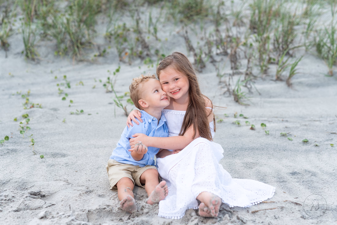 Kids sitting in the sand hugging each other at Huntington Beach State Park