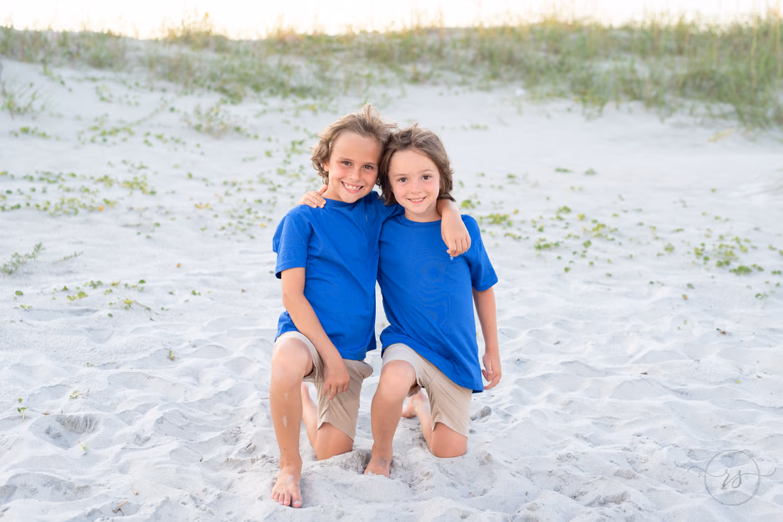 Two boys in matching blue shirts posing on the beach at Huntington Beach State Park