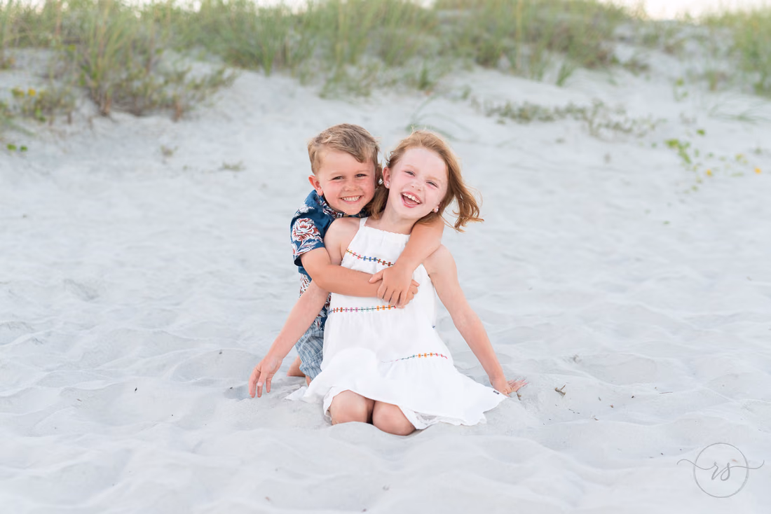 Kids hugging in the sand in front of the dunes at Huntington Beach State Park