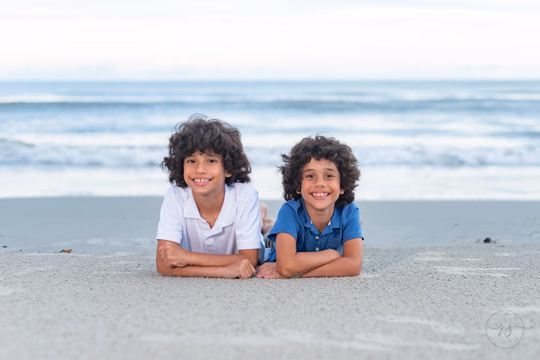 Two boys lying side by side in the sand at Huntington Beach State Park