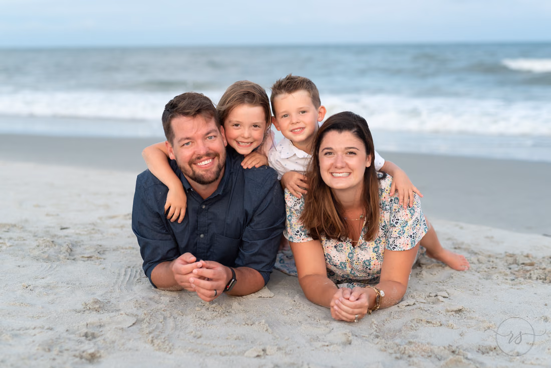Parents lie in the sand as their two kids hug them from behind at Huntington Beach State Park