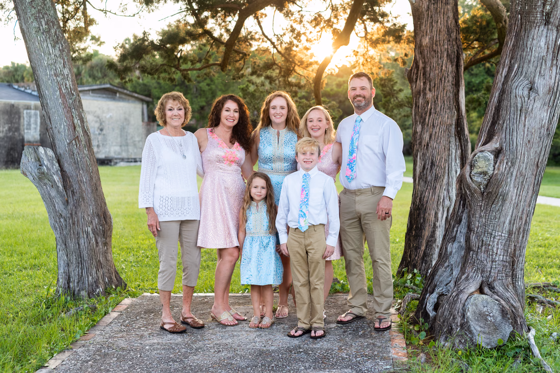 Family in pastel blue and pink standing between two twisted trees at Huntington Beach State Park