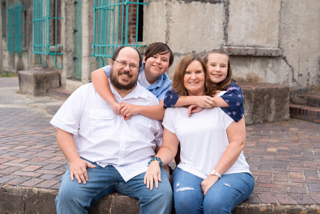 Parents sit on the brick by Atalaya Castle as their two kids hug them from behind at Huntington Beach State Park