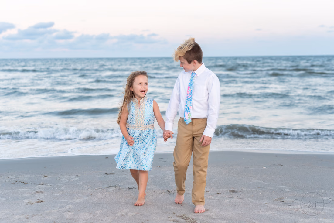 Two kids walking hand in hand along the beach at Huntington Beach State Park