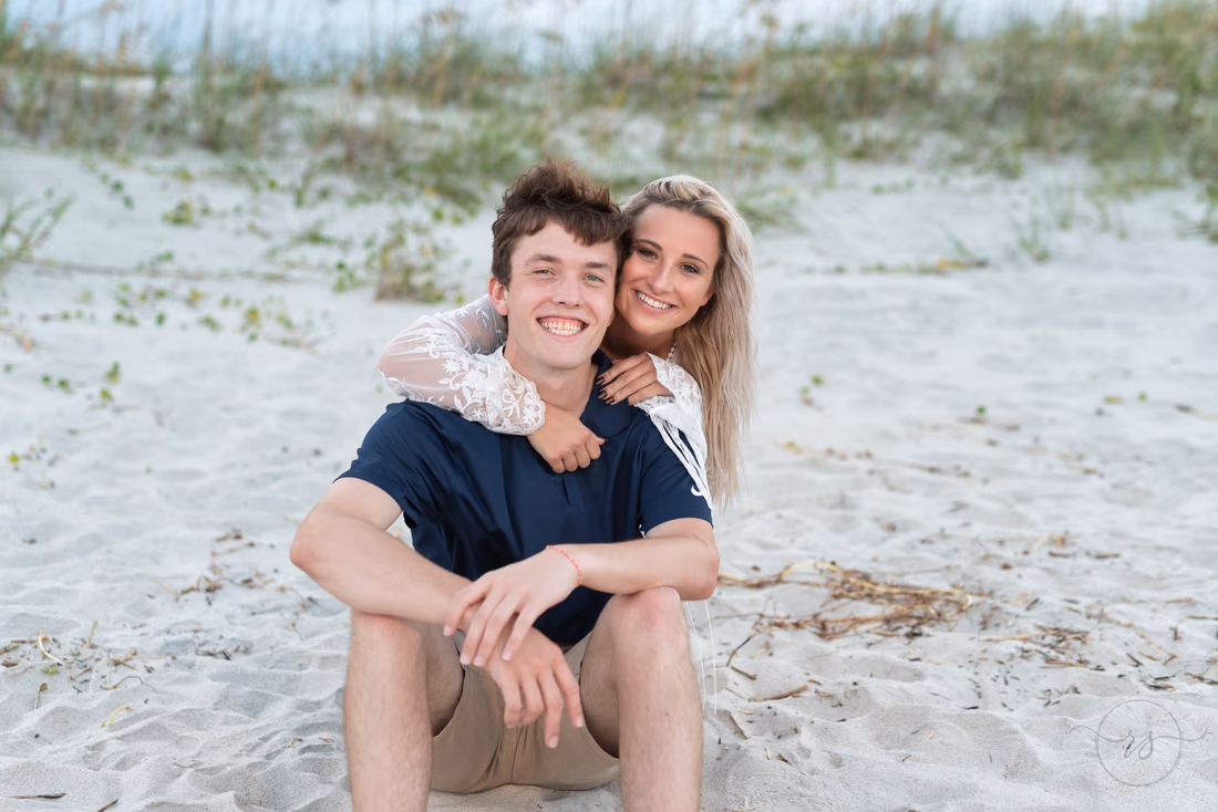 Young man and young woman sitting together in the sand by the dunes at Huntington Beach State Park