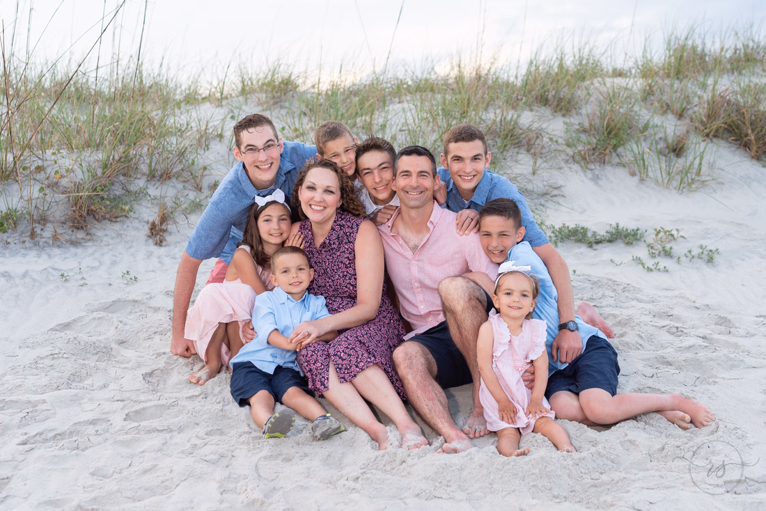 Parents and kids piled together in the sand in front of the dunes at Huntington Beach State Park