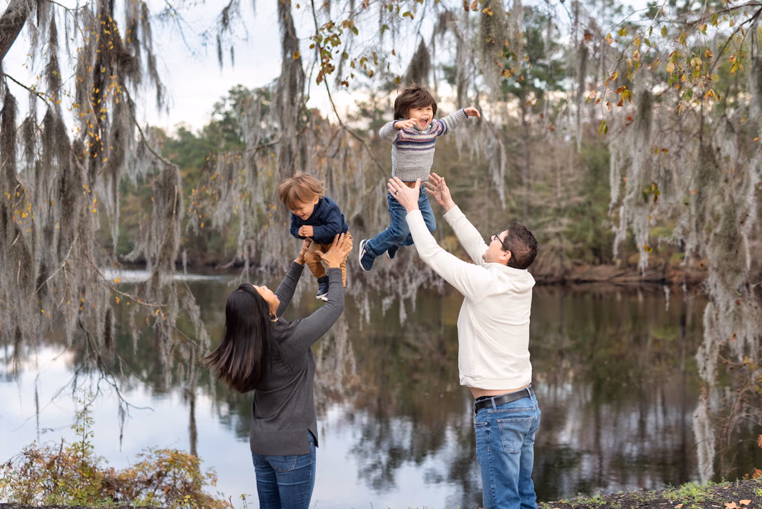 Mom and dad toss their two little boys in the air by the river under Spanish moss at the Conway Riverwalk