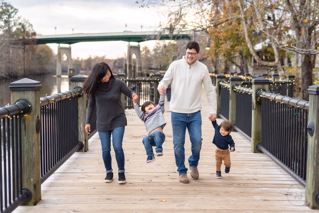Mom and dad swing one little boy between them as the other walks ahead on the boardwalk at the Conway Riverwalk