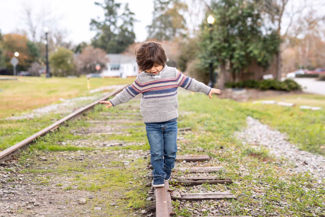 Little boy in a striped sweater balancing on old railroad tracks in Conway