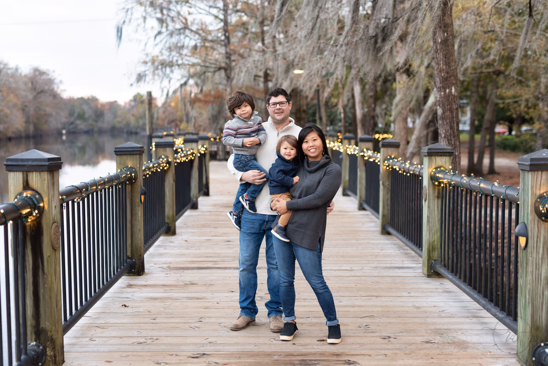 Mom and dad each hold one of their little boys on the boardwalk at the Conway Riverwalk
