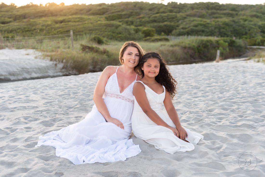 Woman and girl in white sitting together in the sand by the dunes at Myrtle Beach State Park