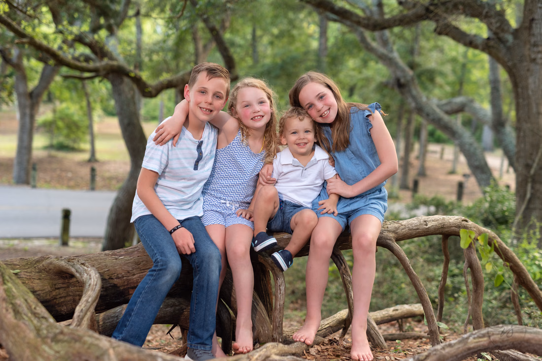 Four kids sitting together on a twisted fallen tree in the woods at Myrtle Beach State Park