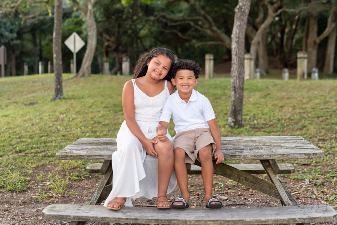 Two kids in white sitting on a picnic table under the trees at Myrtle Beach State Park