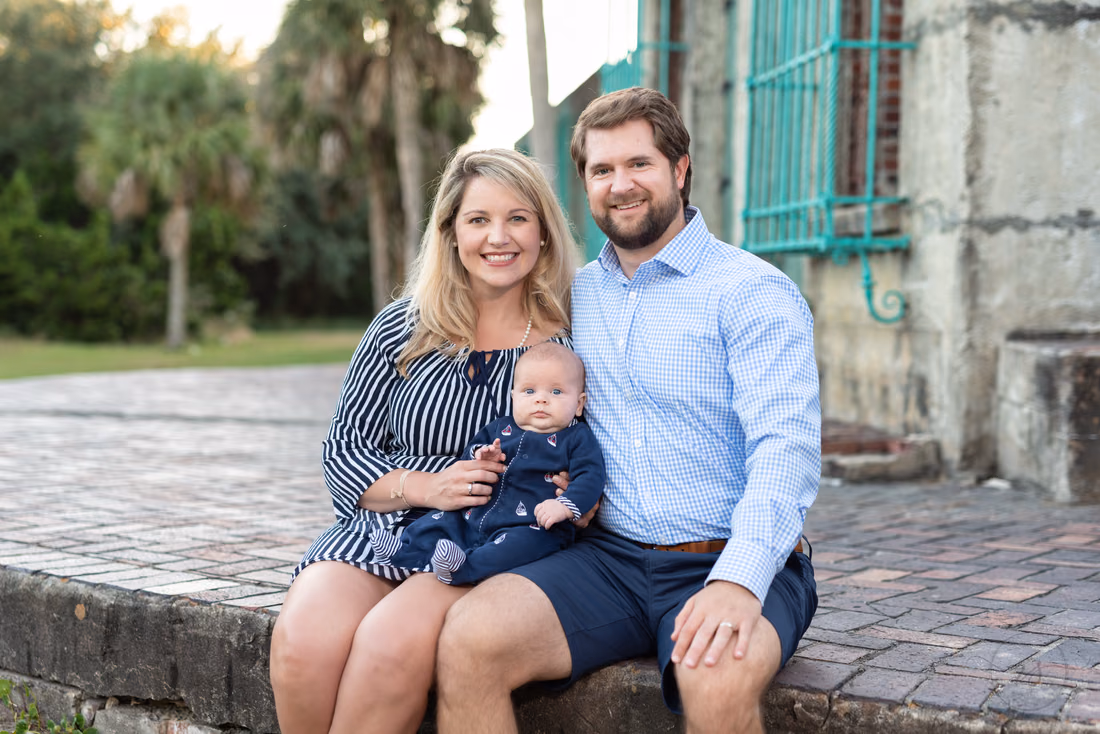 Parents sit on a brick ledge at Atalaya Castle with their baby boy on mom's lap at Huntington Beach State Park
