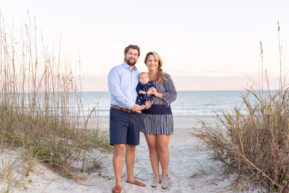 Parents stand between the sea oats on the beach path holding their baby boy at Huntington Beach State Park