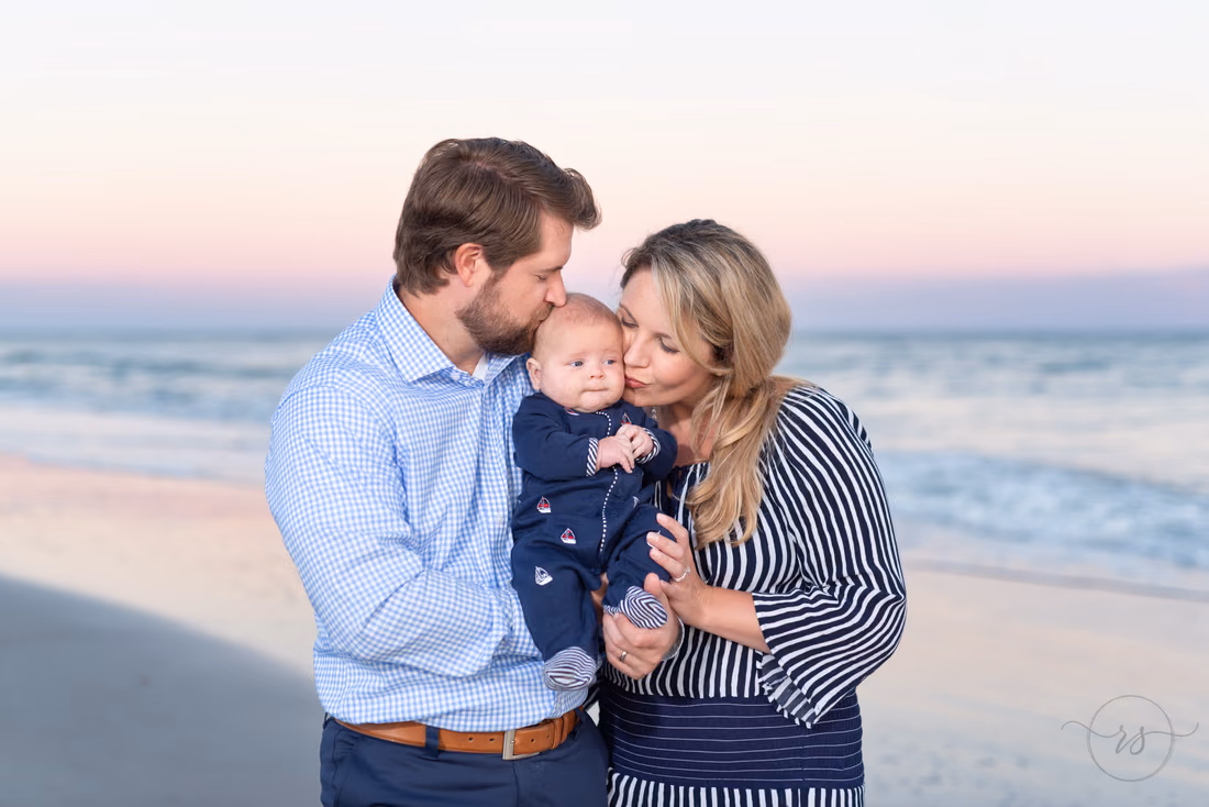 Mom and dad kiss their baby boy by the ocean at sunset at Huntington Beach State Park