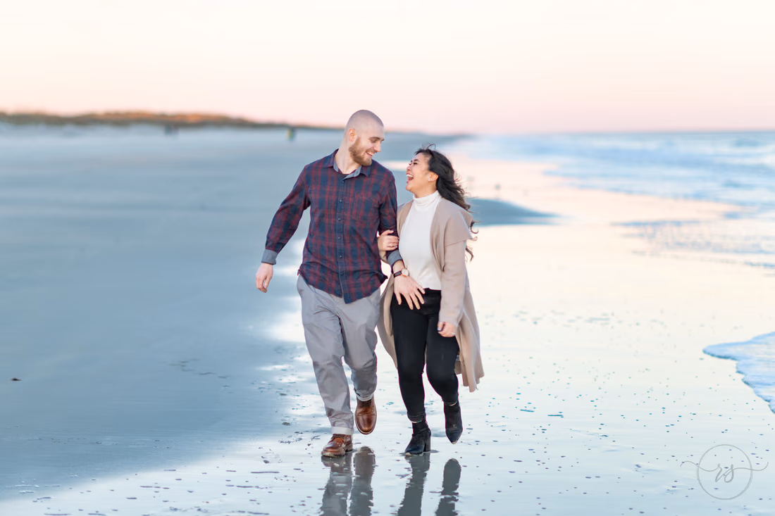 Couple laughing as they walk arm in arm along the shoreline at Huntington Beach State Park