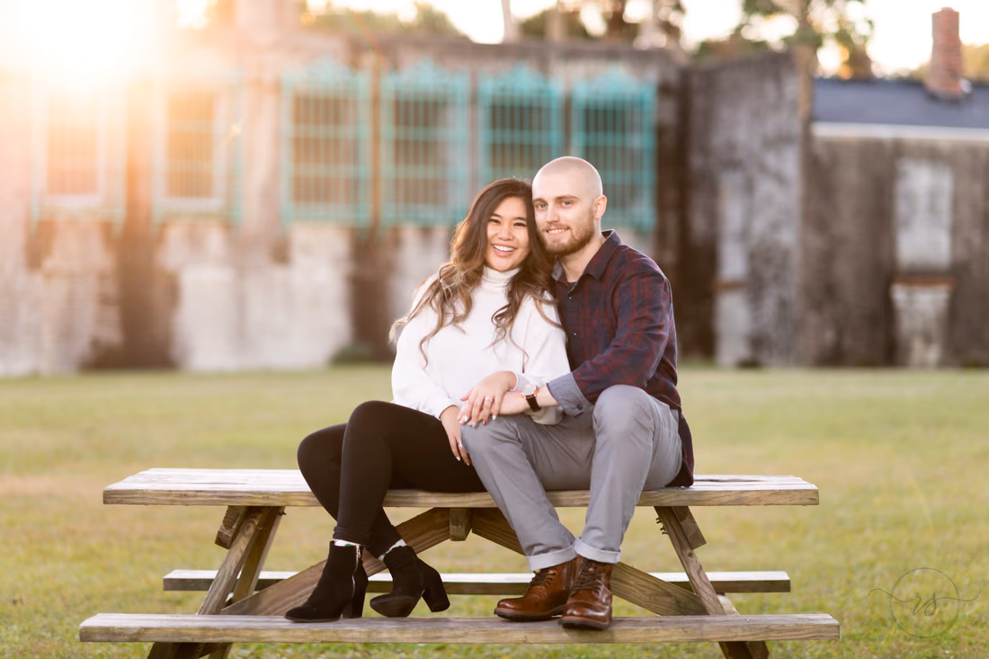 Couple smile on a picnic table as the sun flares behind Atalaya Castle at Huntington Beach State Park