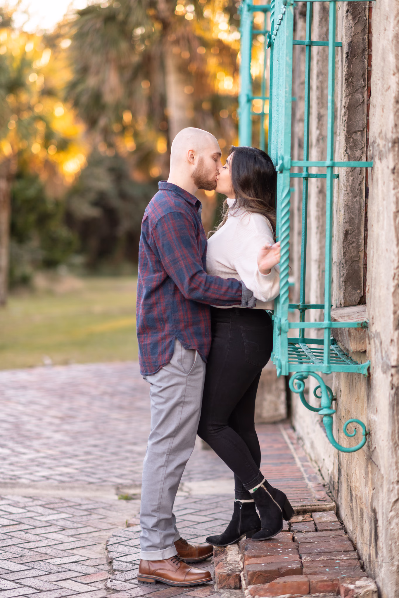 Couple kiss against the castle wall beside a teal wrought iron window at Huntington Beach State Park