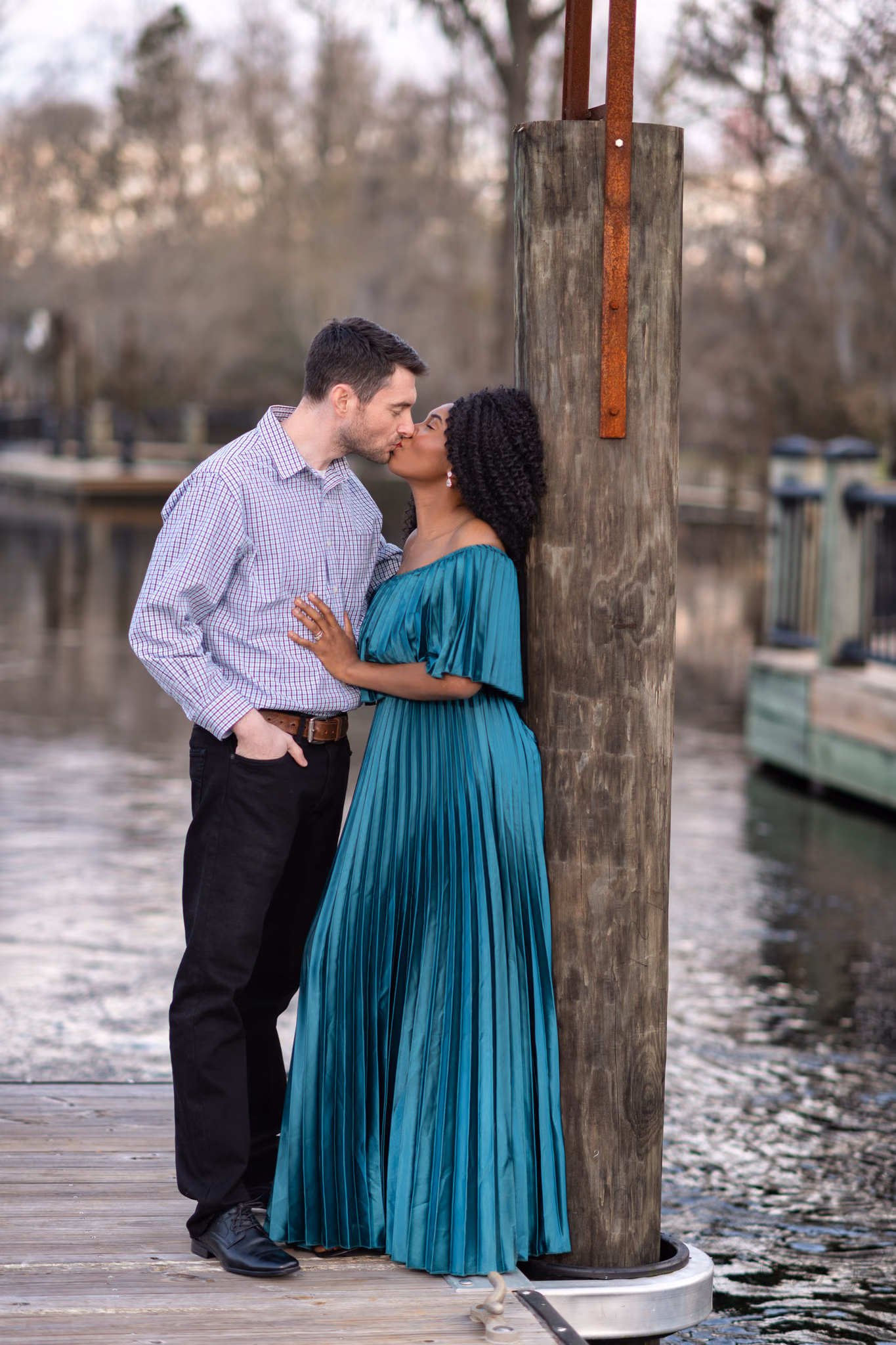 Husband kissing his wife's cheek as she leans on a dock piling at the Conway Riverwalk