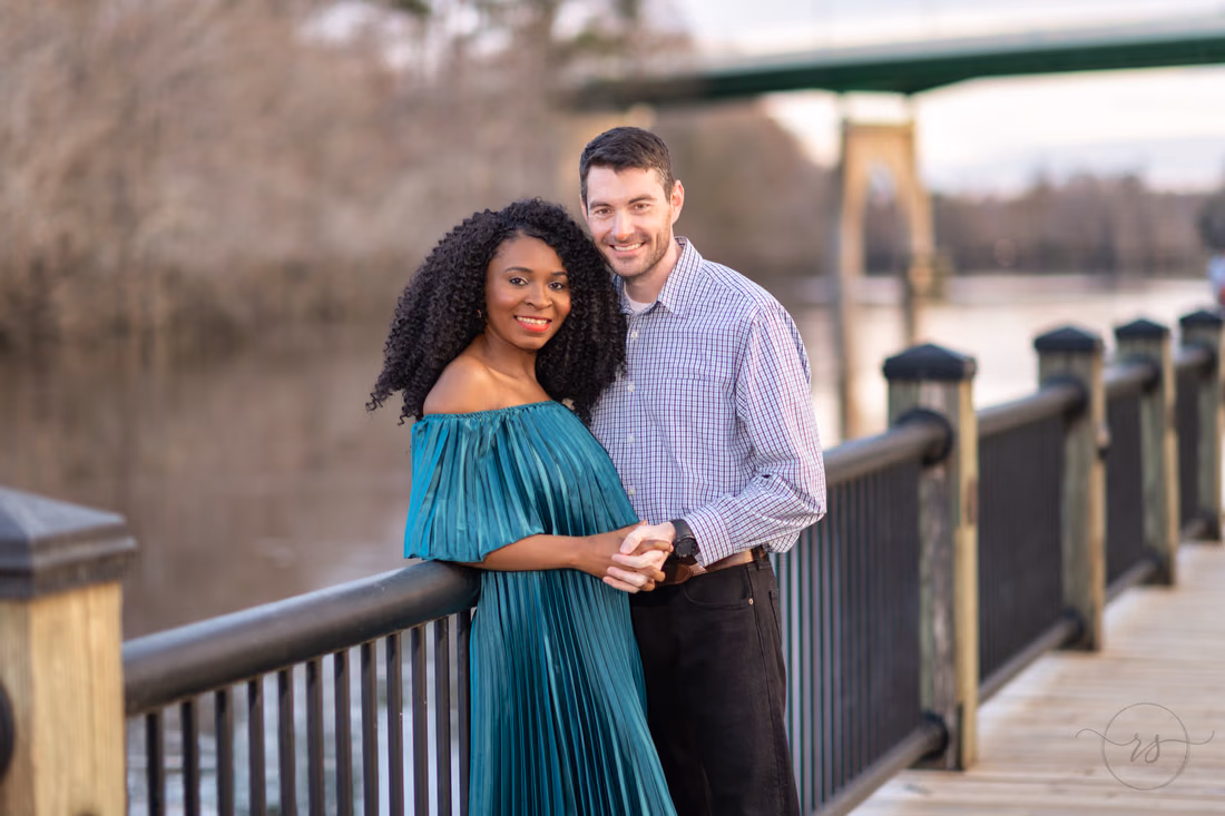 Couple smiling by the boardwalk railing with the river behind them at the Conway Riverwalk
