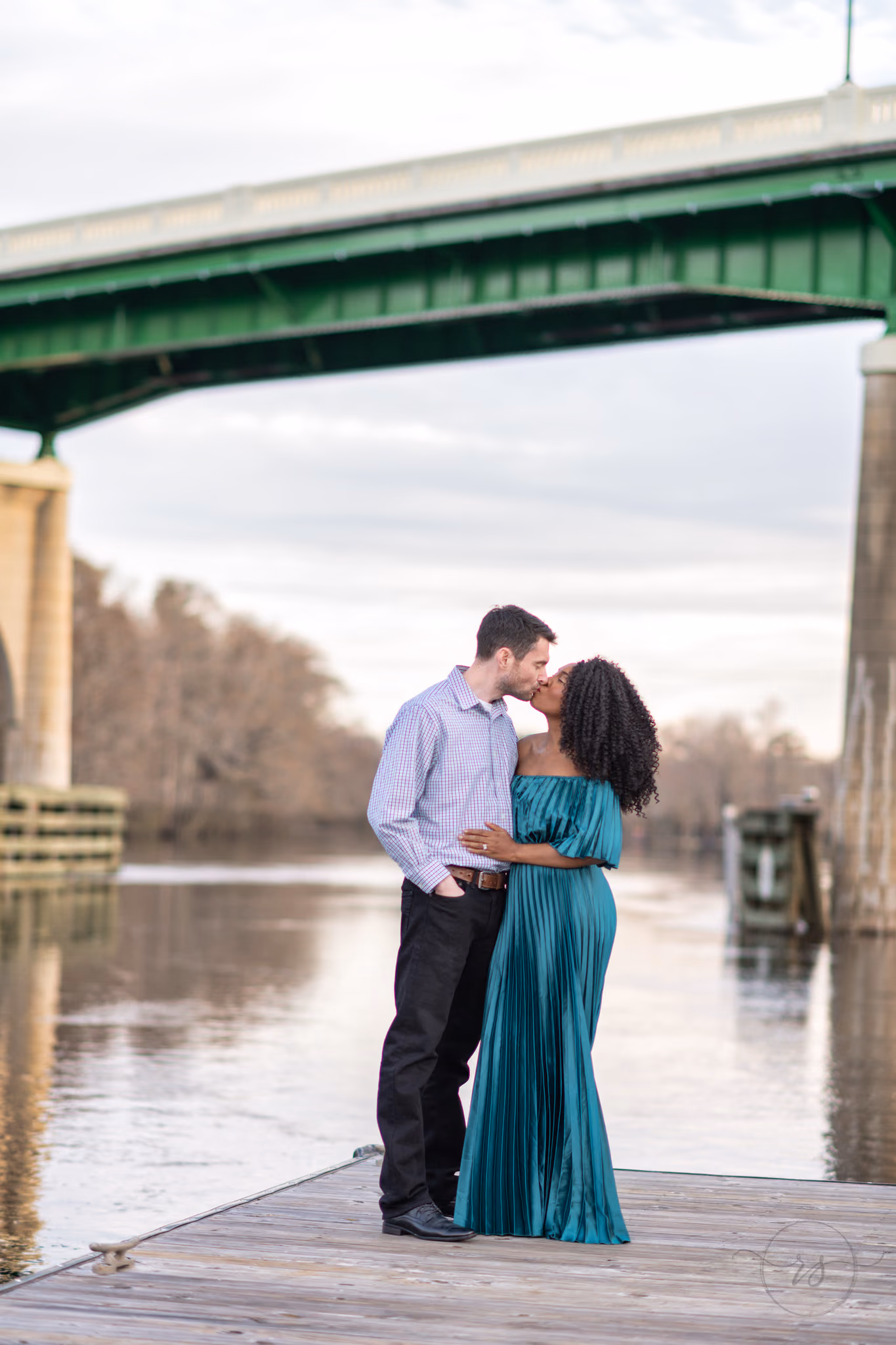 Couple kissing on the river dock with the bridge overhead at the Conway Riverwalk