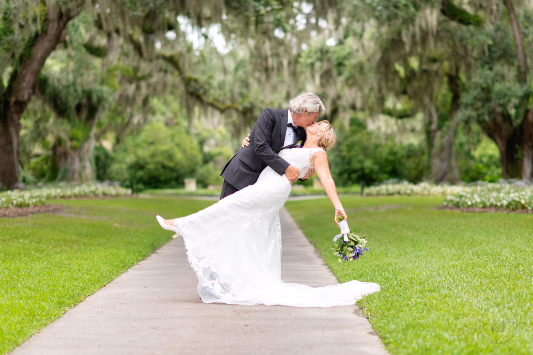 Bride kicking up her leg as the groom dips her for a kiss under the Live Oak Allee at Brookgreen Gardens