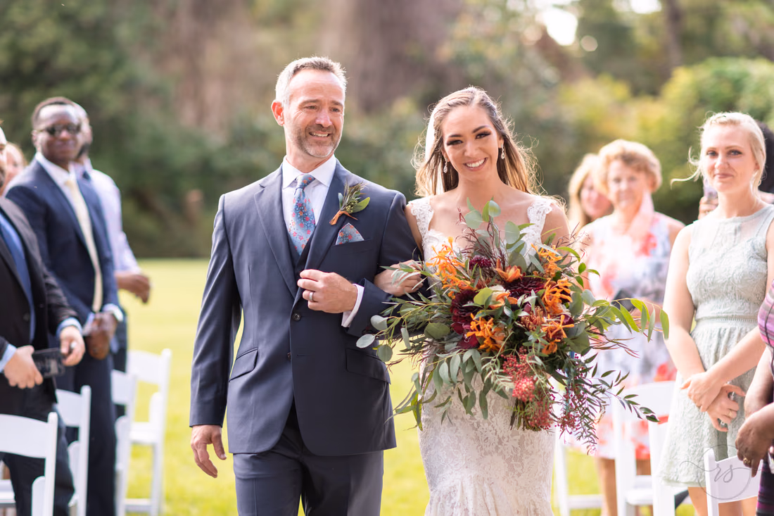 Bride smiles as her father walks her down the aisle on the lawn at Magnolia Plantation