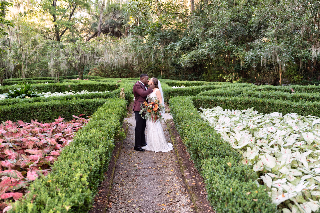 Bride and groom kiss on the garden path between the hedges at Magnolia Plantation
