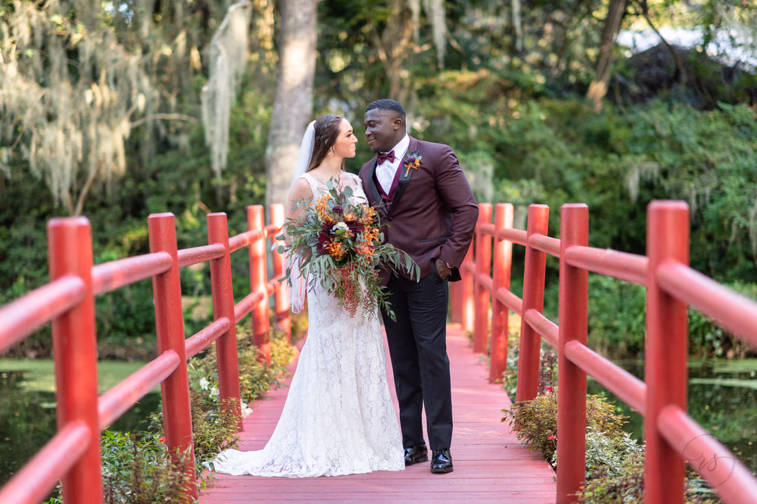 Bride and groom smile at each other on the red bridge at Magnolia Plantation