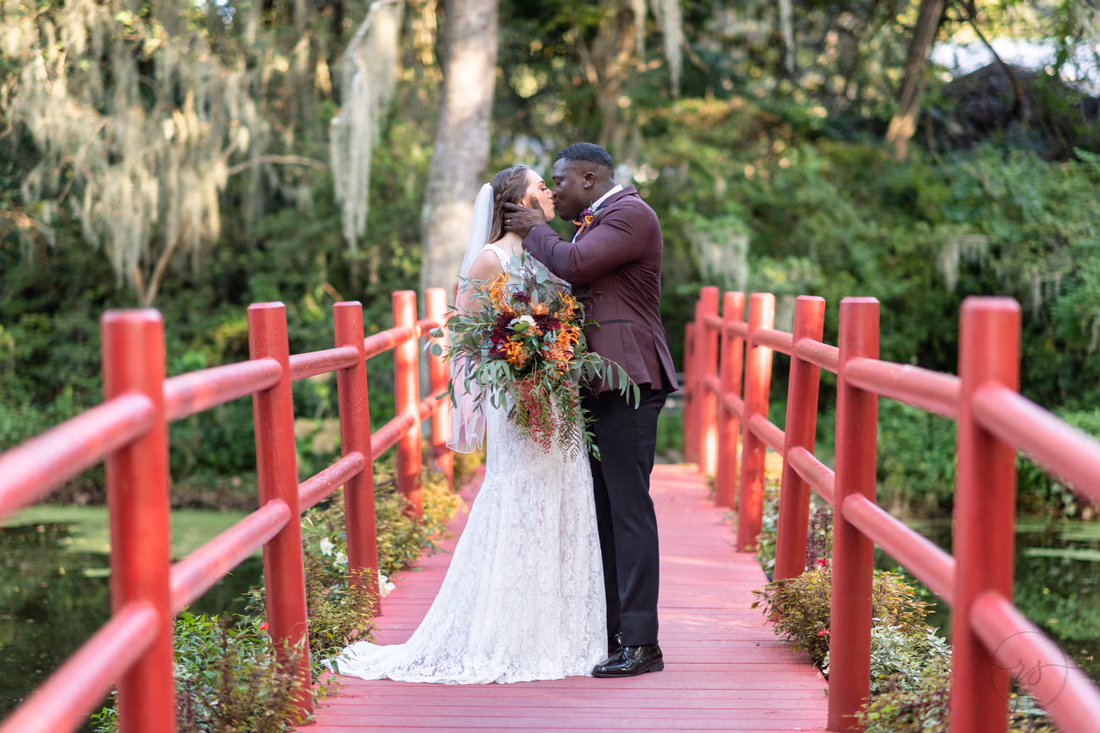 Bride and groom kiss on the red bridge at Magnolia Plantation
