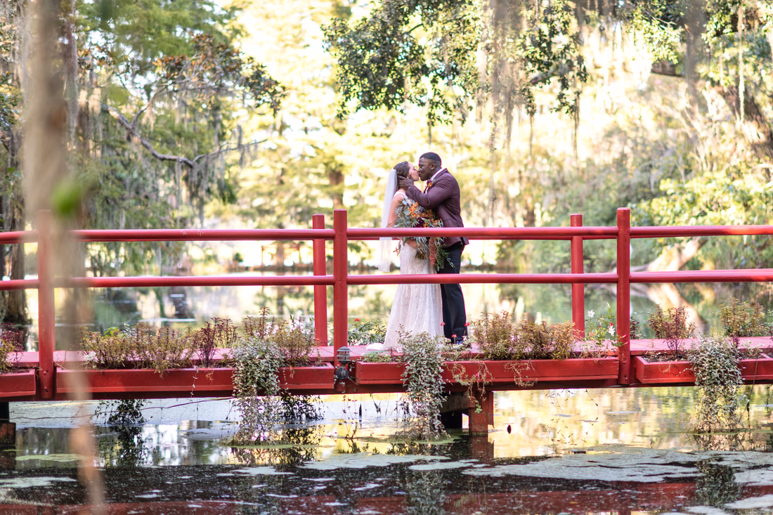 Bride and groom kiss on the red bridge above the pond at Magnolia Plantation